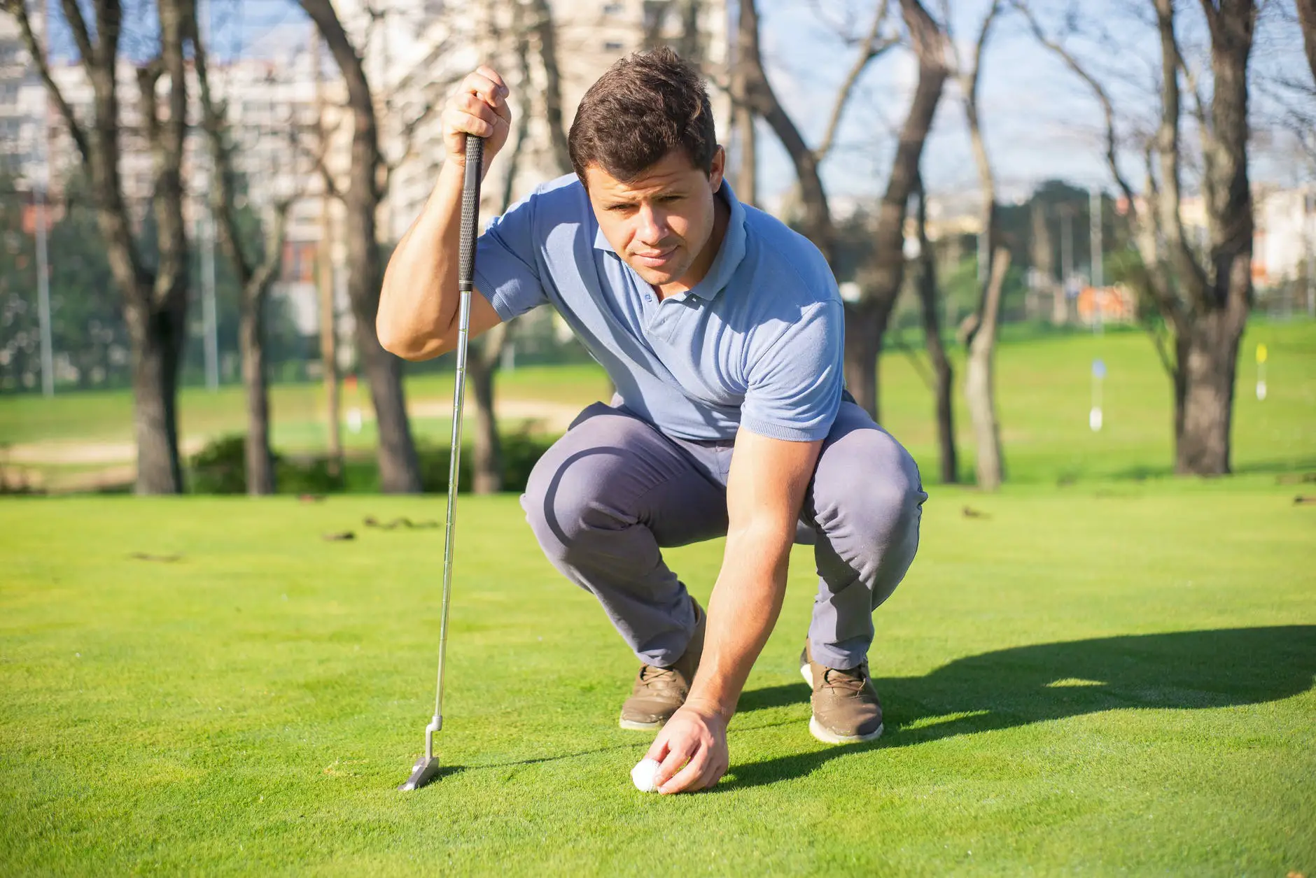 a man sitting on green grass while holding a golf club and a ball