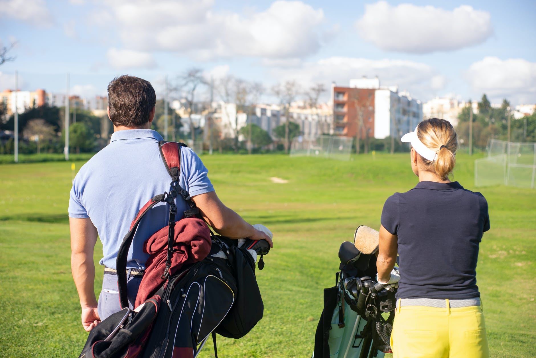 a back view of a man and woman carrying golf equipments